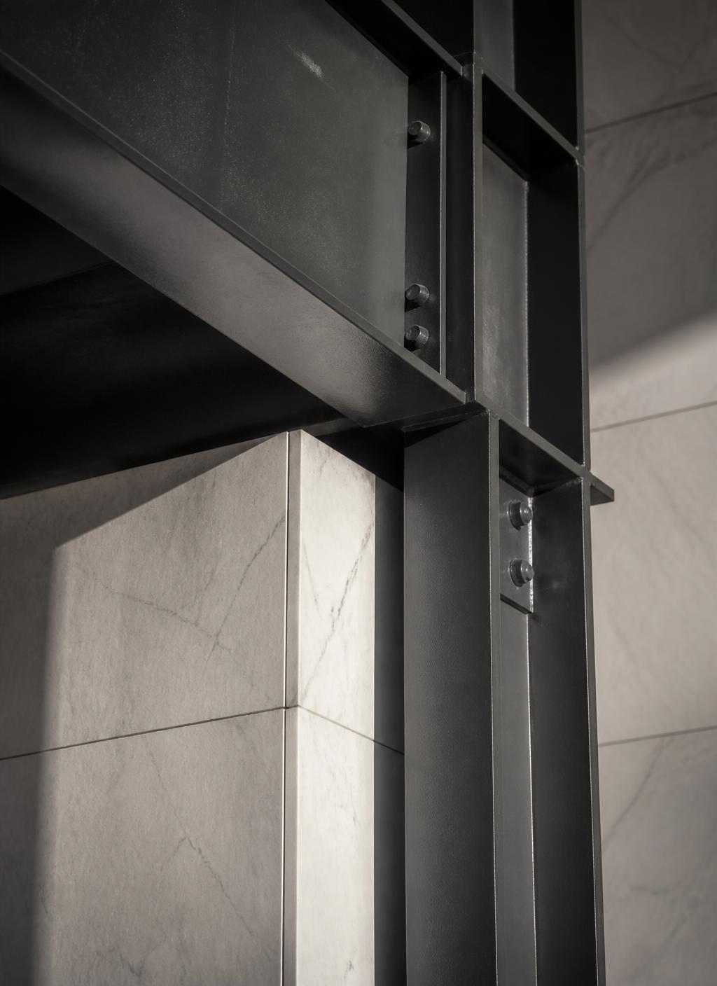 Marble cladding meeting a dark steel structural column in raking light